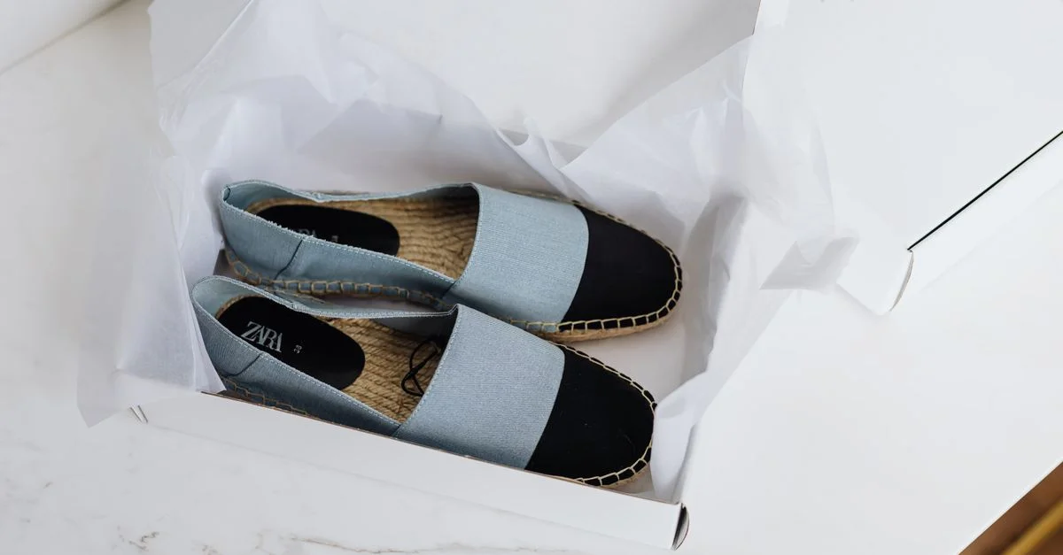 Stylish espadrilles bleues et noires soigneusement emballées dans une boîte blanche sur une table en marbre.