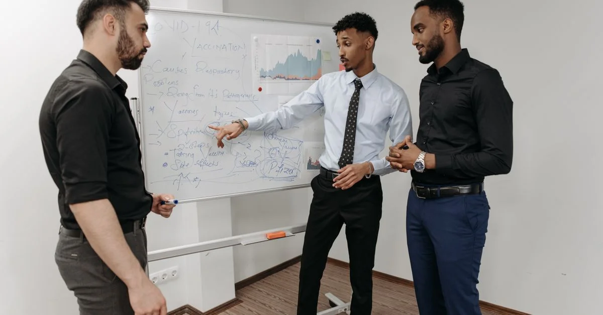 Trois professionnels discutant de stratégies devant un tableau blanc dans un cadre de bureau.