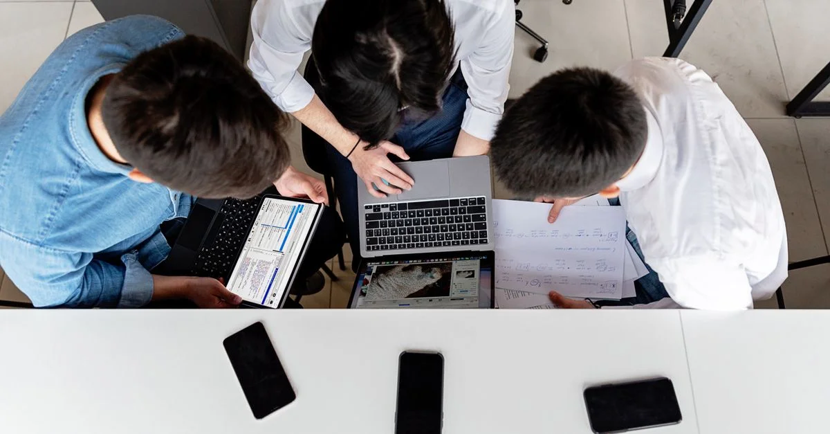 Trois collègues travaillant ensemble sur des ordinateurs portables à un bureau avec des documents.